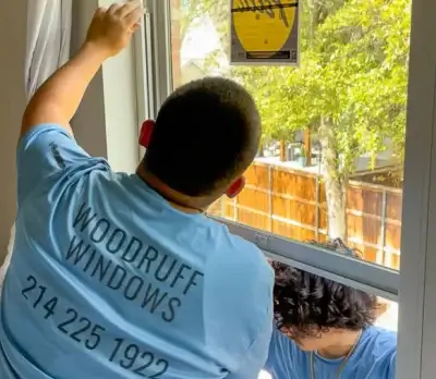 Two workers in blue Woodruff Windows shirts install a window sticker while working on an open window.