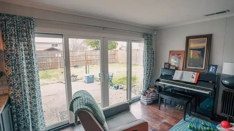 A cozy room with a chair, piano, and large sliding glass doors opening to a fenced backyard.