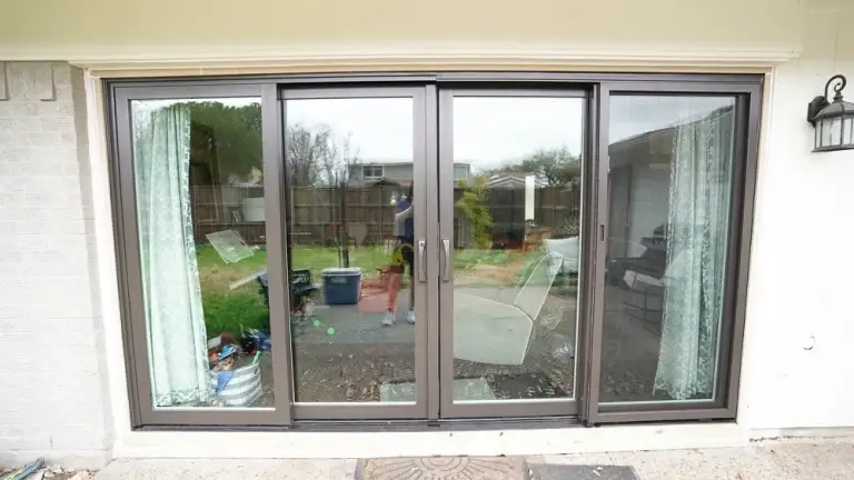Large glass sliding patio doors with black frames and white curtains, leading to a backyard with a fence and greenery.