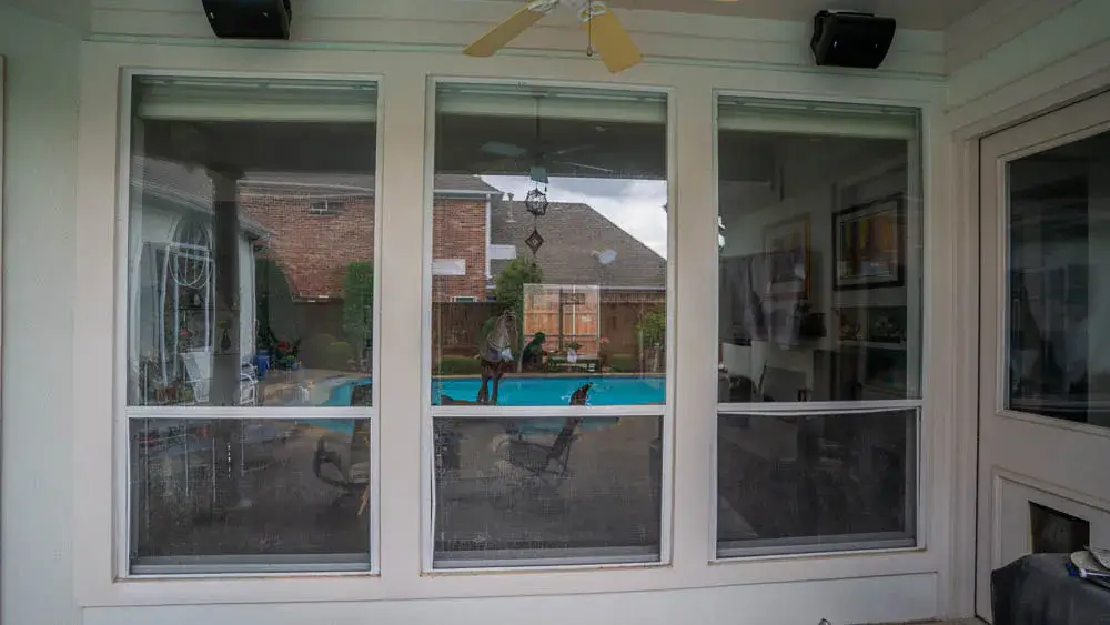 Three large windows look out onto a backyard with a pool, brick wall, and patio furniture visible outside.