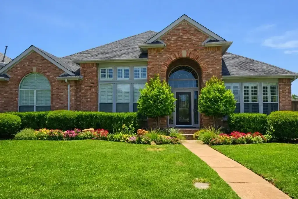 Single-story brick house with large windows, landscaped garden, green lawn, and a concrete walkway leading to the front door.