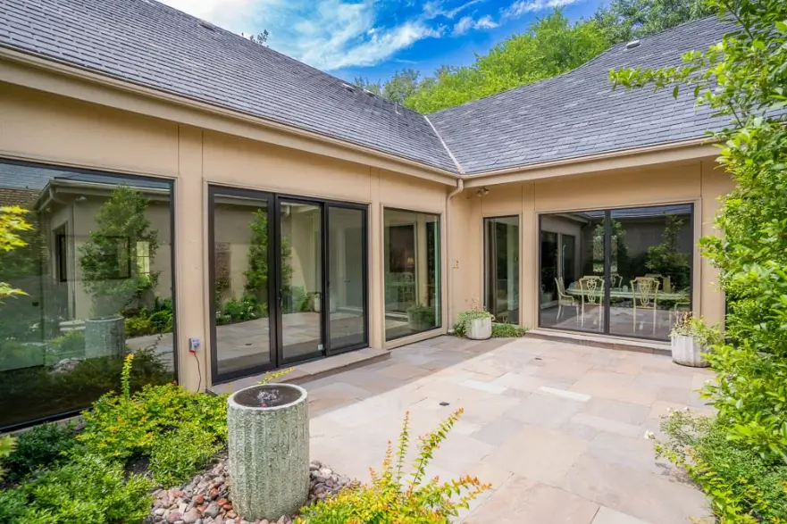 Sunny courtyard with large glass doors, potted plants, stone tiles, and greenery surrounding the area.