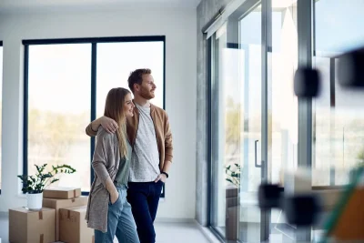 A couple looking through large high-performance windows in their home, evaluating natural light and energy efficiency after window replacement